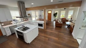Cozinha espaçosa com ilha central, piso de madeira e área de jantar com sofá de couro marrom.