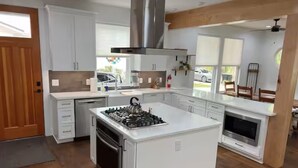 Uma cozinha moderna com armários brancos, uma ilha central com fogão e micro-ondas embutido.
