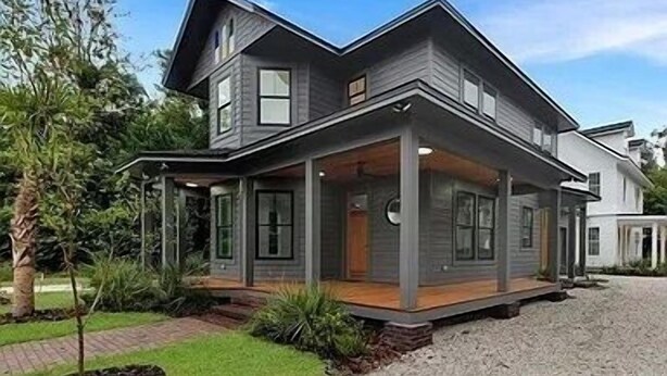 Uma casa moderna de dois andares com varanda coberta, entrada de cascalho e um jardim bem cuidado.