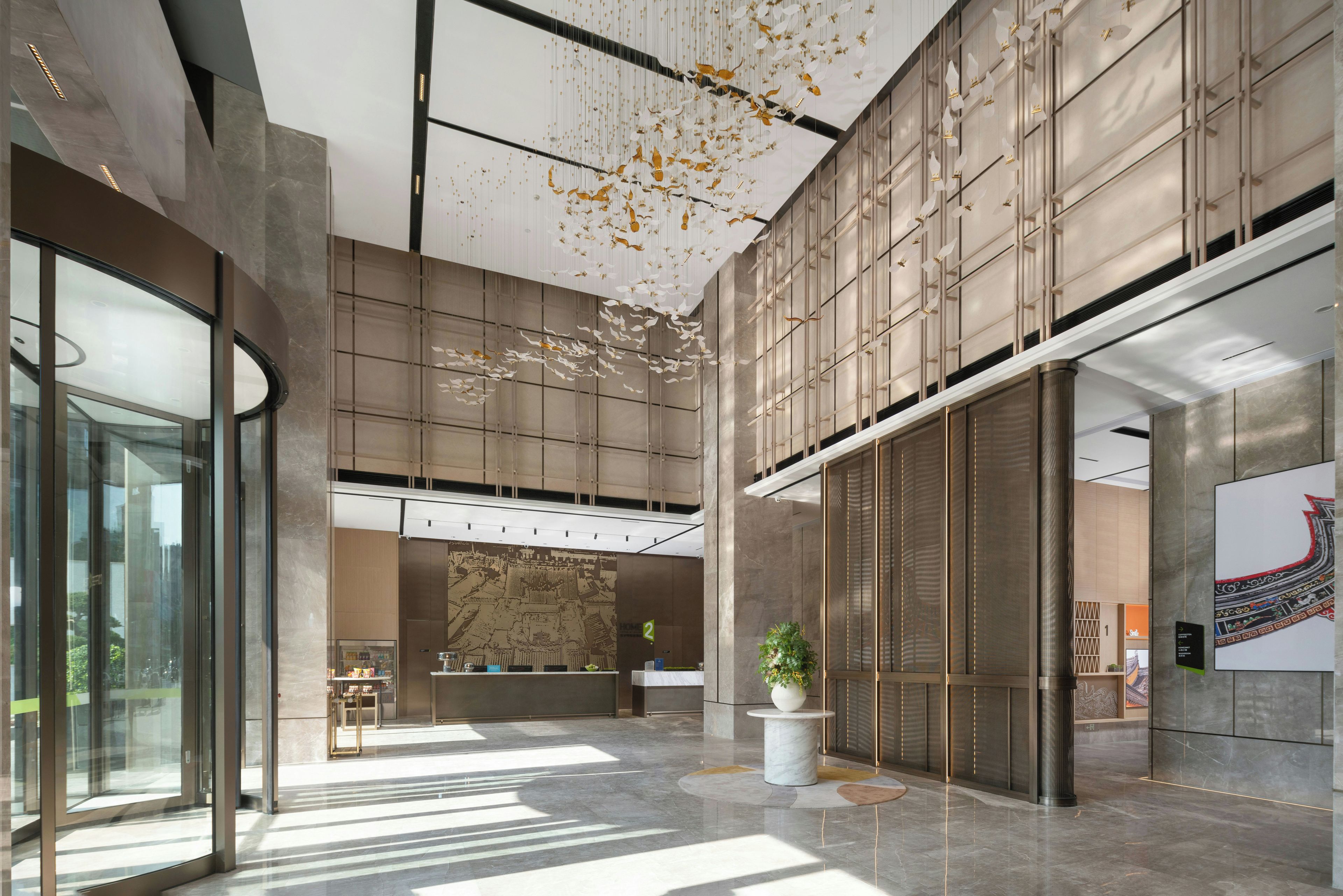 A spacious lobby with a reception desk, a large plant, and a modern design with a high ceiling and patterned walls.