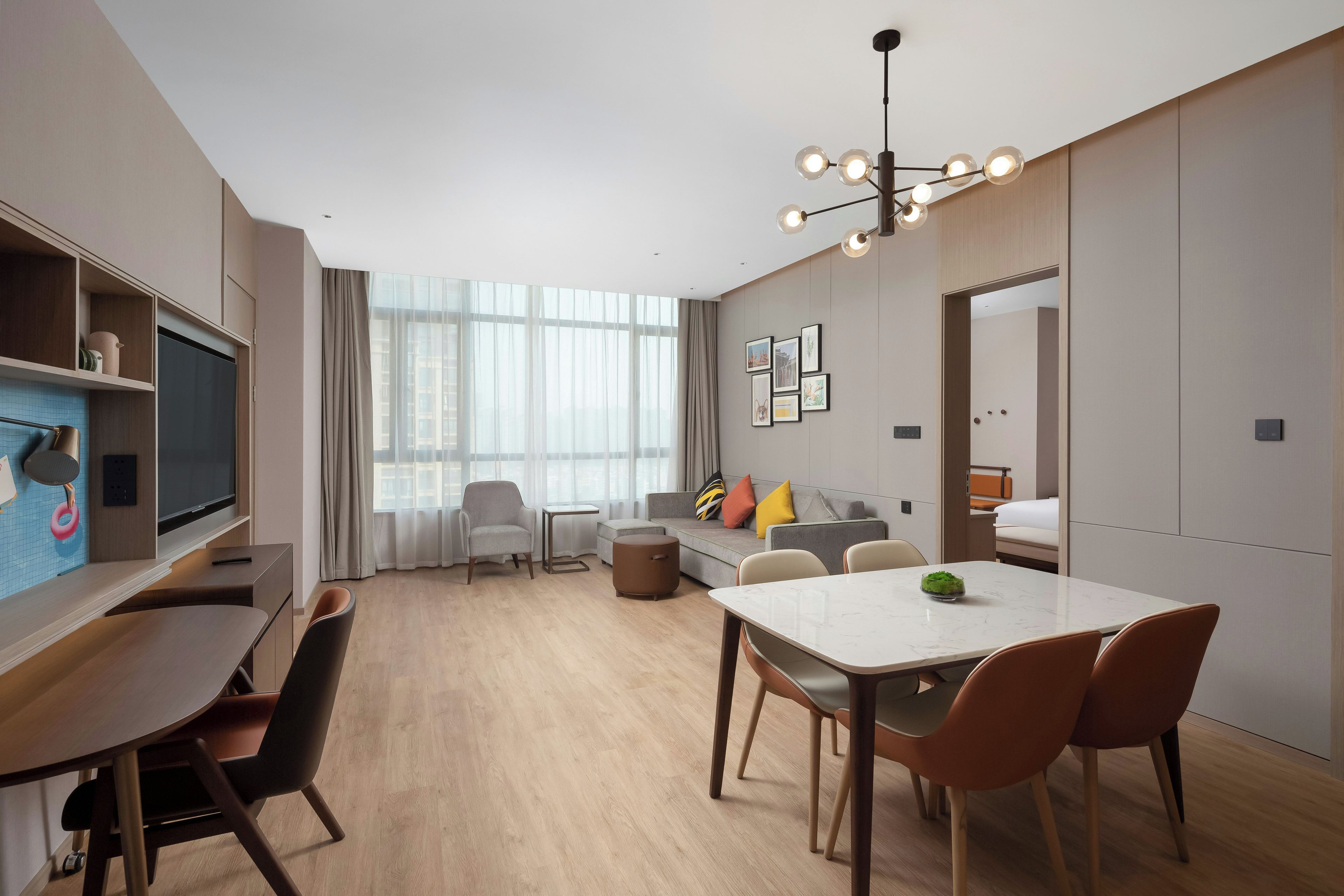 Een moderne hotelkamer met een zithoek, een bank, een televisie en een groot raam met gordijnen.