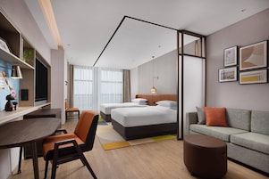 Quarto de hotel moderno com cama, sofá, escrivaninha e área de jantar.