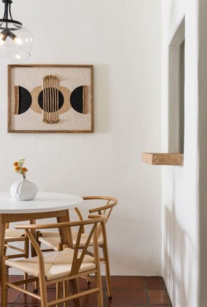 Un comedor con una mesa redonda, dos sillas, un florero con flores y una obra de arte colgada en la pared.