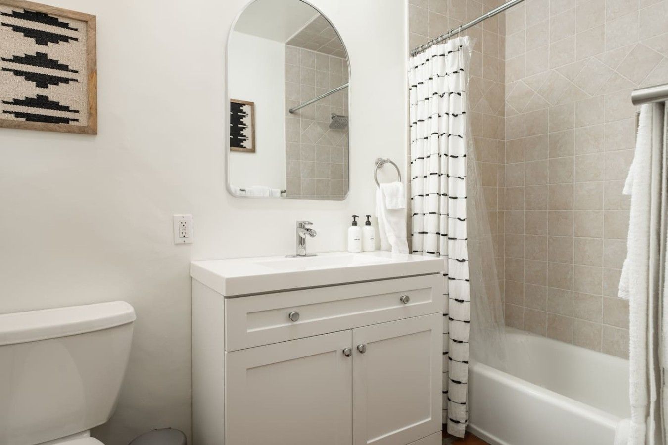 A bathroom with a toilet, a sink with a mirror above it, a shower with a curtain, and a towel hanging on the wall.