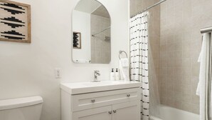 Ein Badezimmer mit Toilette, einem Waschbecken mit Spiegel darüber, einer Duschkabine und einem Handtuch an der Wand.