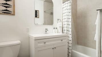 A bathroom with a toilet, a sink with a mirror above it, a shower with a curtain, and a towel hanging on the wall.