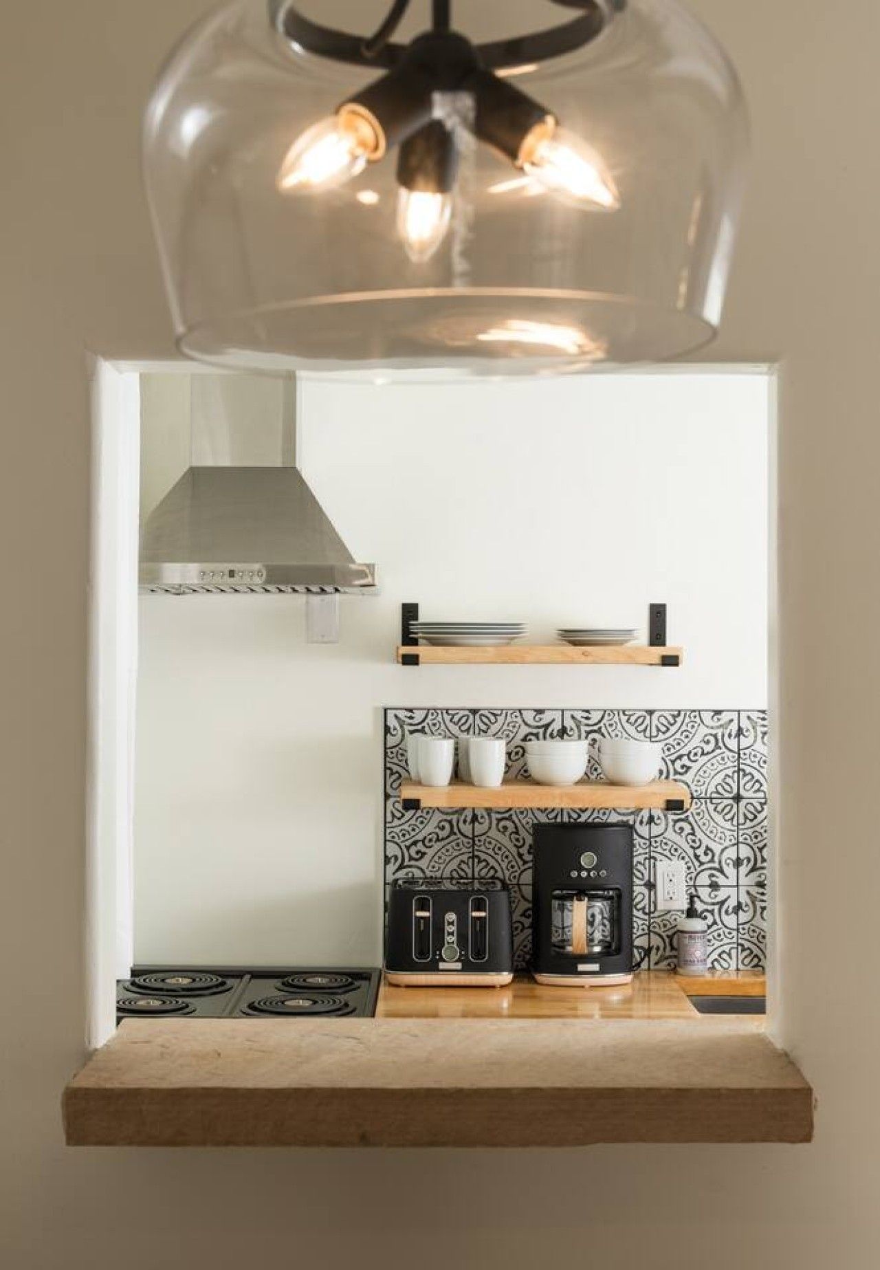 A kitchen with a modern design, featuring a built-in stove, a coffee maker, and a hanging light fixture above the counter.