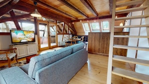 A loft-style room with a wooden ceiling, a large window, a television, a sofa, and a dining area. - manala 2 gite a turckheim (Turckheim)