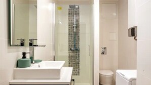 Un bany modern amb un espai de banyera de vidre, un lavabo blanc i un dosificador de sabó verd, i un vàter blanc.