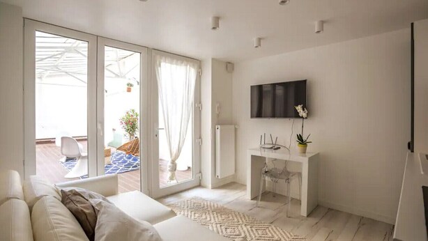 Un saló modern amb un sofà, un televisor fixat a la paret i una porta corredissa de vidre que dona a una zona exterior.