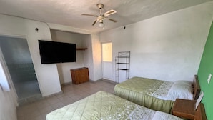 A room with two beds, a ceiling fan, a TV mounted on the wall, and a small wooden cabinet.