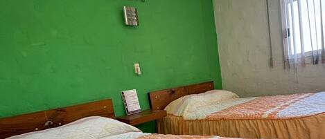 Una habitación con dos camas, cada una con colcha de estampado floral, un aire acondicionado de pared y una ventana con barrotes.