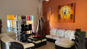 A living room with a sofa, a coffee table, and a bookshelf. There is a painting on the wall and a window with blinds.