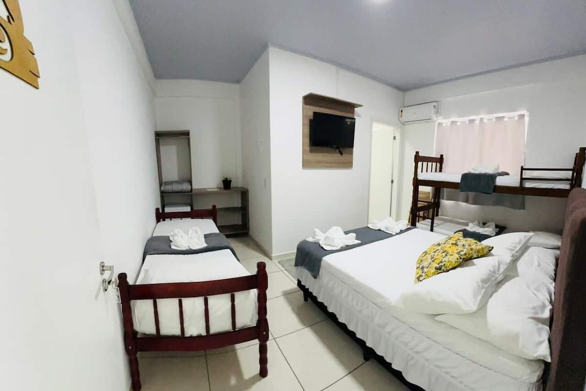 Quarto de hotel com duas camas de solteiro, cabeceira de madeira, televisão fixada na parede e janela com cortinas.