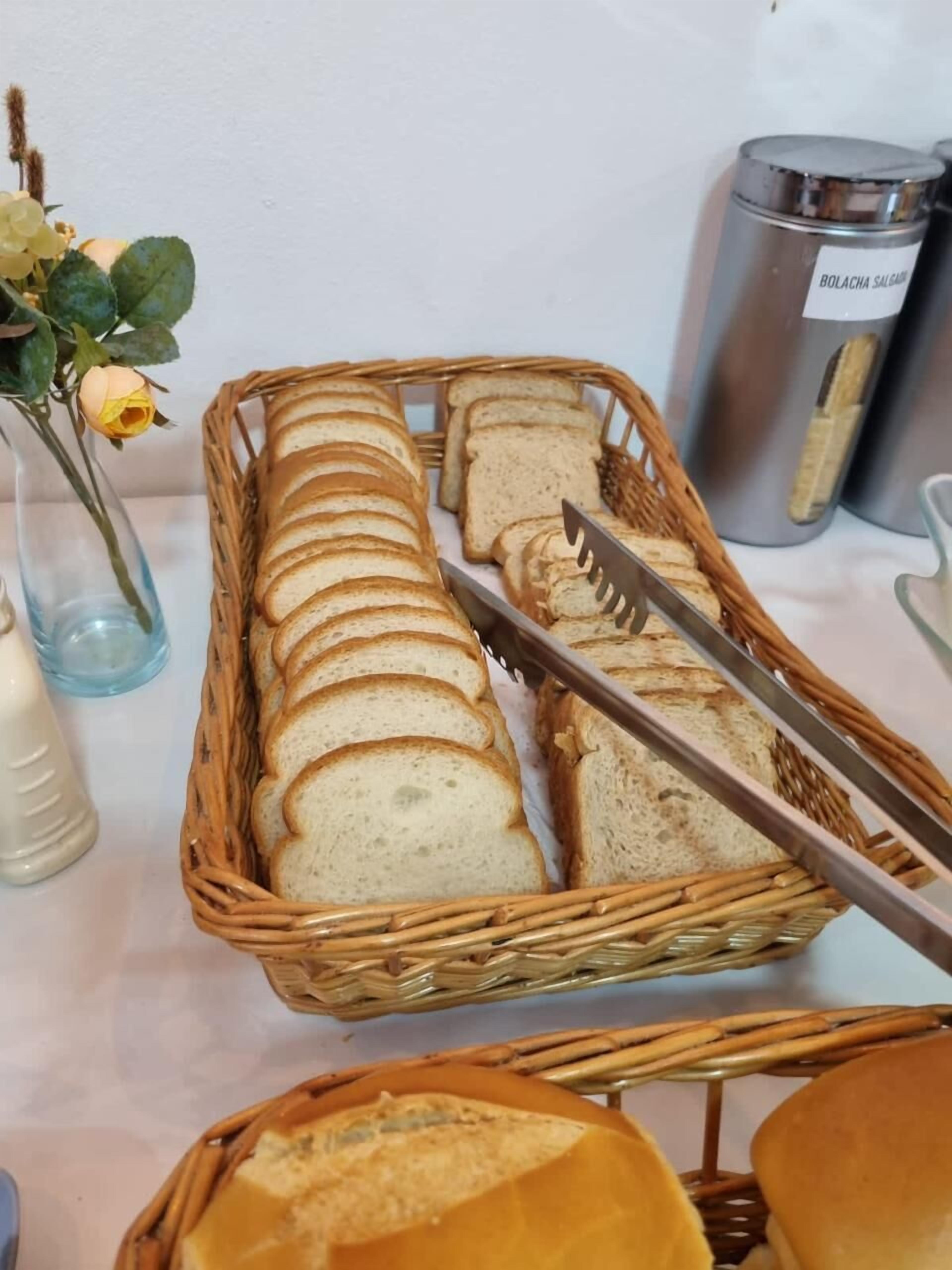 Una mesa de buffet con pan en cestas de mimbre, un cuchillo y un bote etiquetado como 'BOLACHA SALSA'.
