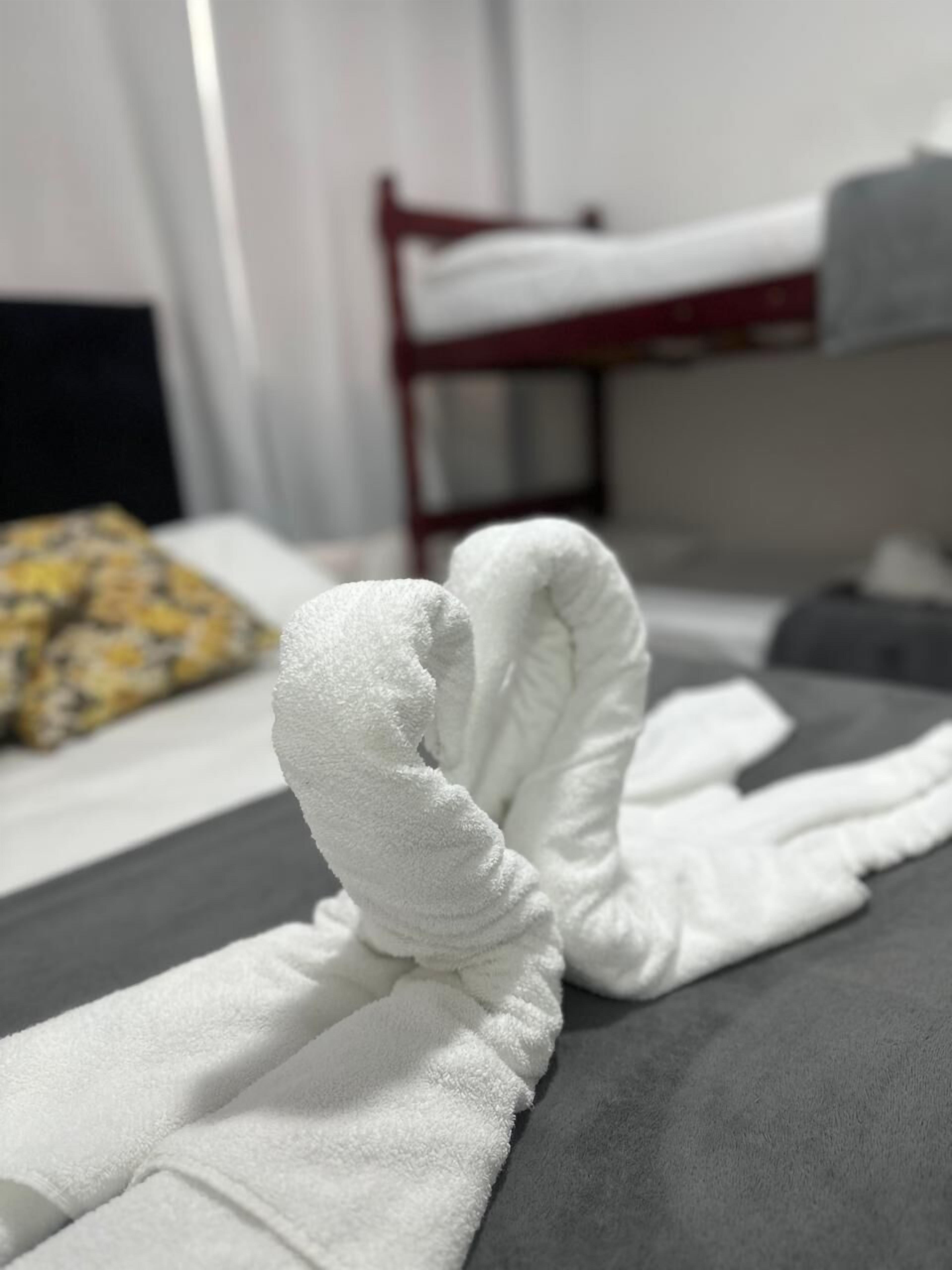 A neatly made white towel on a bed with a gray mattress and a red headboard.