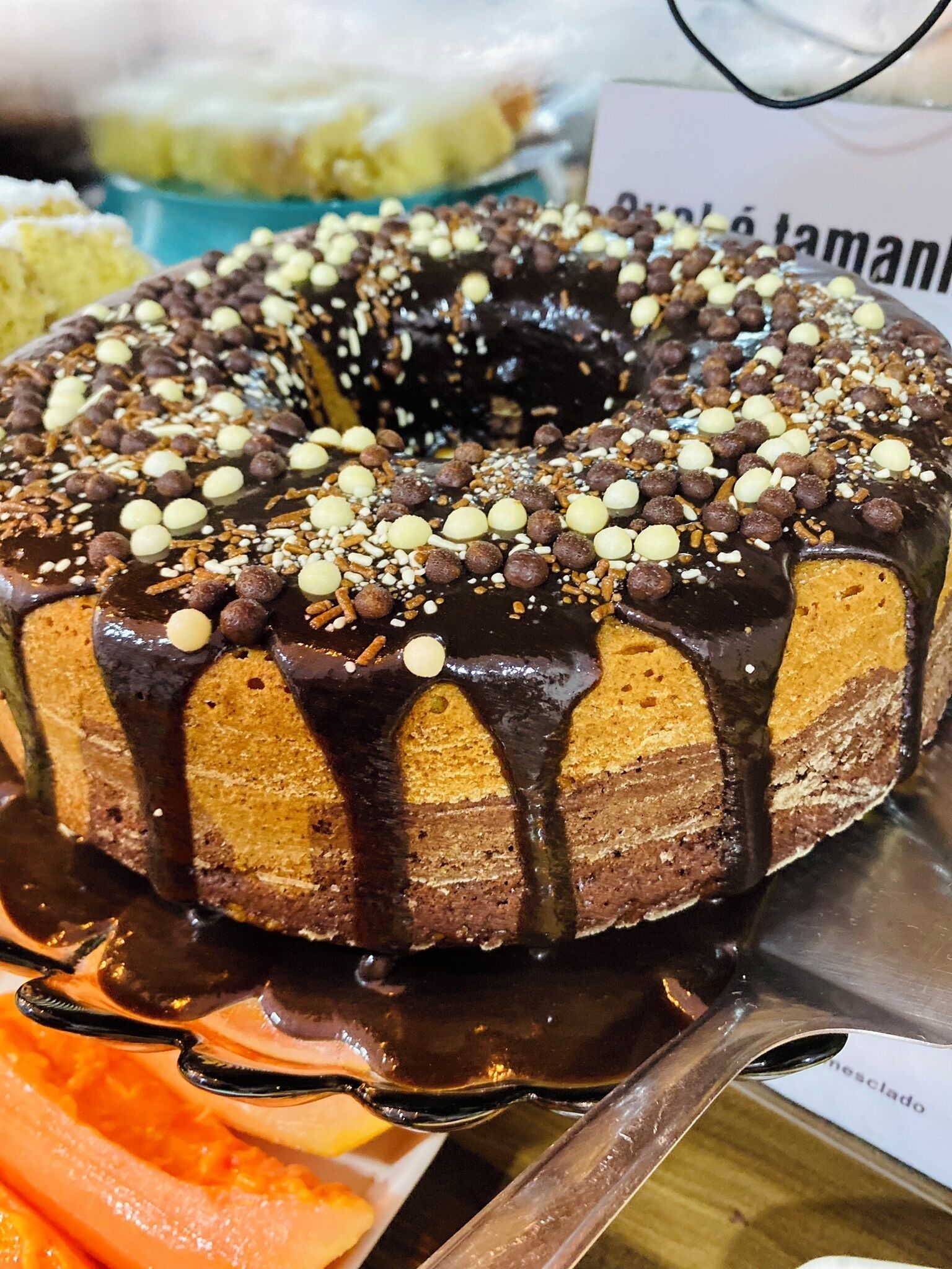 A chocolate-glazed bundt cake with nuts and chocolate chips on a serving tray.