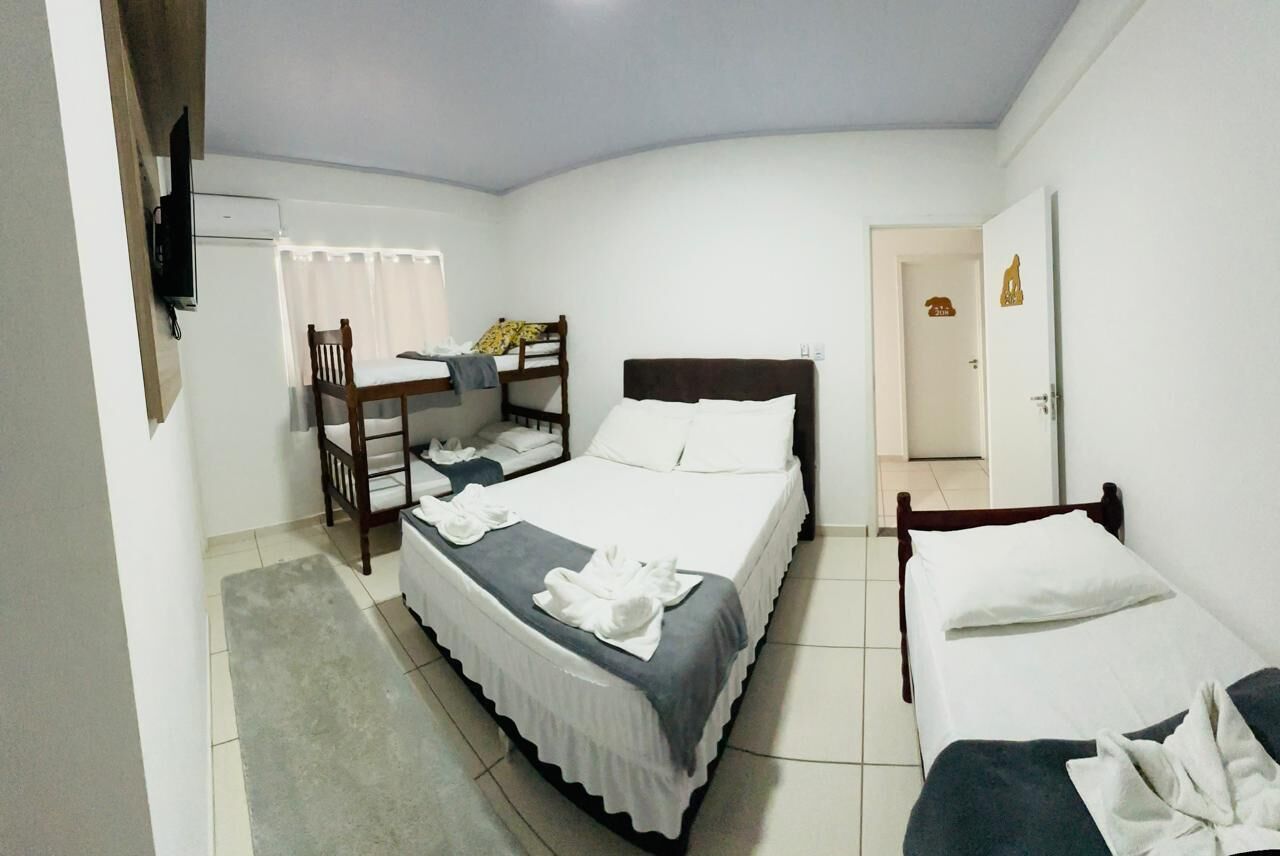 Une chambre avec un lit superposé, un lit simple, un bureau avec une chaise et un téléviseur fixé au mur.