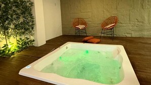 A hot tub in a room with wooden flooring and two wicker chairs. - Pousada Safari (Penha)