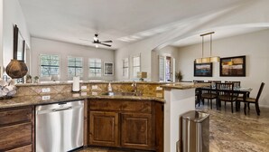 A kitchen with a dishwasher, wooden cabinets, a marble countertop, and a dining area with chairs and a table.
