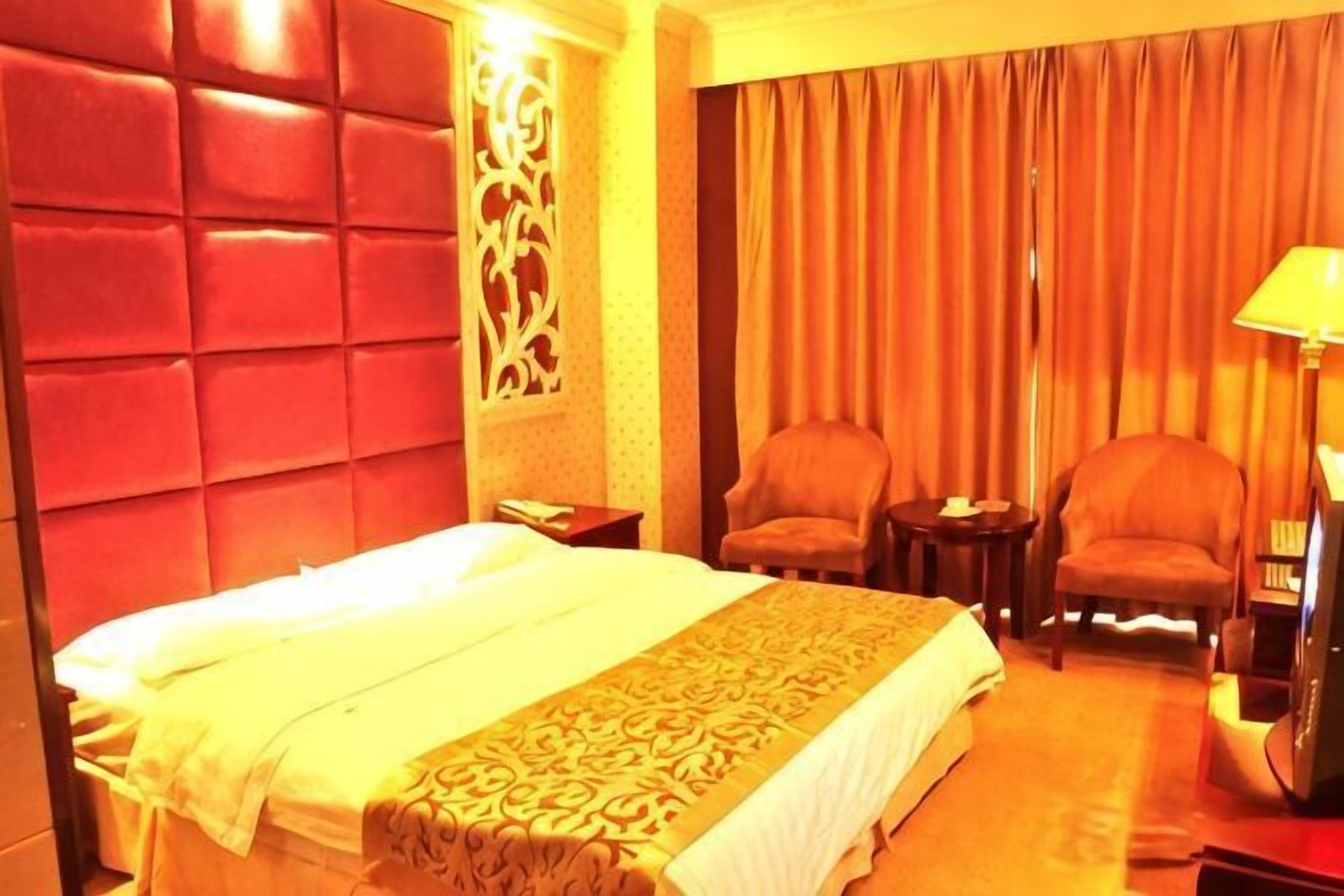 A hotel room with a large bed, two armchairs, a nightstand, and a lamp.
