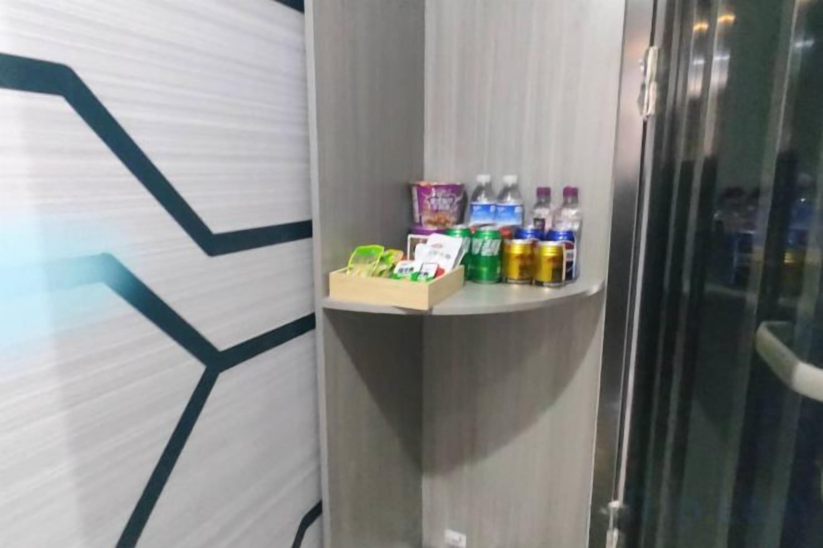 A corner of a room with a shelf holding various bottled beverages and a small box of tissues.