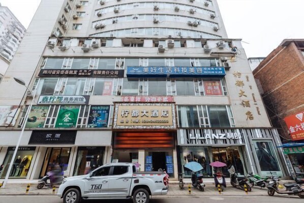 Un edificio de varios pisos con diversos comercios en la planta baja, incluyendo un hotel, una peluquería de belleza tecnológica y una tienda con un letrero llamativo.