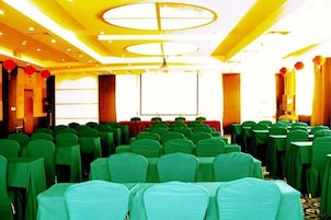 Un salón de conferencias con filas de sillas, una pantalla de proyector y un escenario.