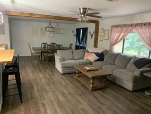 Relax in this inviting living room with a large sofa, dining area, and ceiling fan.