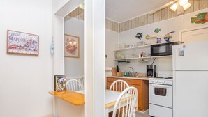 A compact kitchen with white cabinetry, a microwave, a stove, and a refrigerator. There is a wooden bench and a dining table with chairs. - 2 Bedroom w Porch Overlooking all the fun! (Kure Beach)