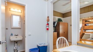 A compact room with a sink, a fire extinguisher, a trash bin, a wooden table, and a bunk bed. - 2 Bedroom w Porch Overlooking all the fun! (Kure Beach)