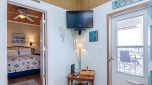 A bedroom with a bed, a television mounted on the wall, a small table with a lamp, and a door leading to an outdoor area. - 2 Bedroom w Porch Overlooking all the fun! (Kure Beach)