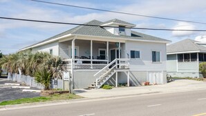A single-story house with a porch, a staircase leading to the entrance, and a small attached garage. - 2 Bedroom w Porch Overlooking all the fun! (Kure Beach)