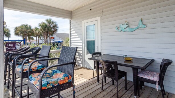 A covered outdoor patio with wicker furniture and a table, a sign for 'Big Daddy's', and a decorative mermaid mural on the wall. - 2 Bedroom w Porch Overlooking all the fun! (Kure Beach)