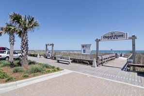 A wooden boardwalk leading to Ocean Front Park with benches and a sign.