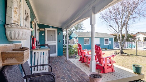 Une véranda avec des fauteuils Adirondack rouges, une petite table et une porte blanche.