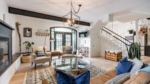 Un salón espacioso con una mesa de centro redonda de cristal, un sofá con cojines azules, una chimenea y una escalera que sube a un nivel superior.