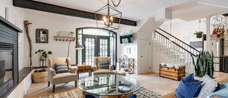 A spacious living room with a round glass coffee table, a sofa with blue cushions, a fireplace, and a staircase leading to an upper level.