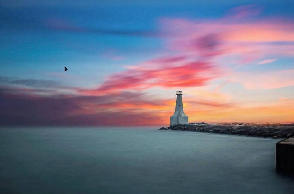 Un phare perché sur un promontoire rocheux, avec une mer calme et un ciel au coucher du soleil aux couleurs éclatantes.