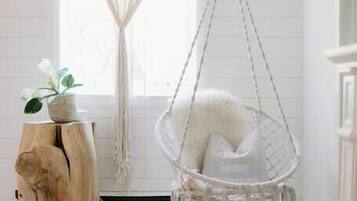 Ein Zimmer mit Hängesessel, Holzschemel mit Pflanze und weißer Wand mit Fenster.