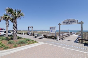 A wooden boardwalk leading to Ocean Front Park with benches and a sign.