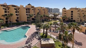 A resort with a swimming pool, palm trees, and yellow buildings.