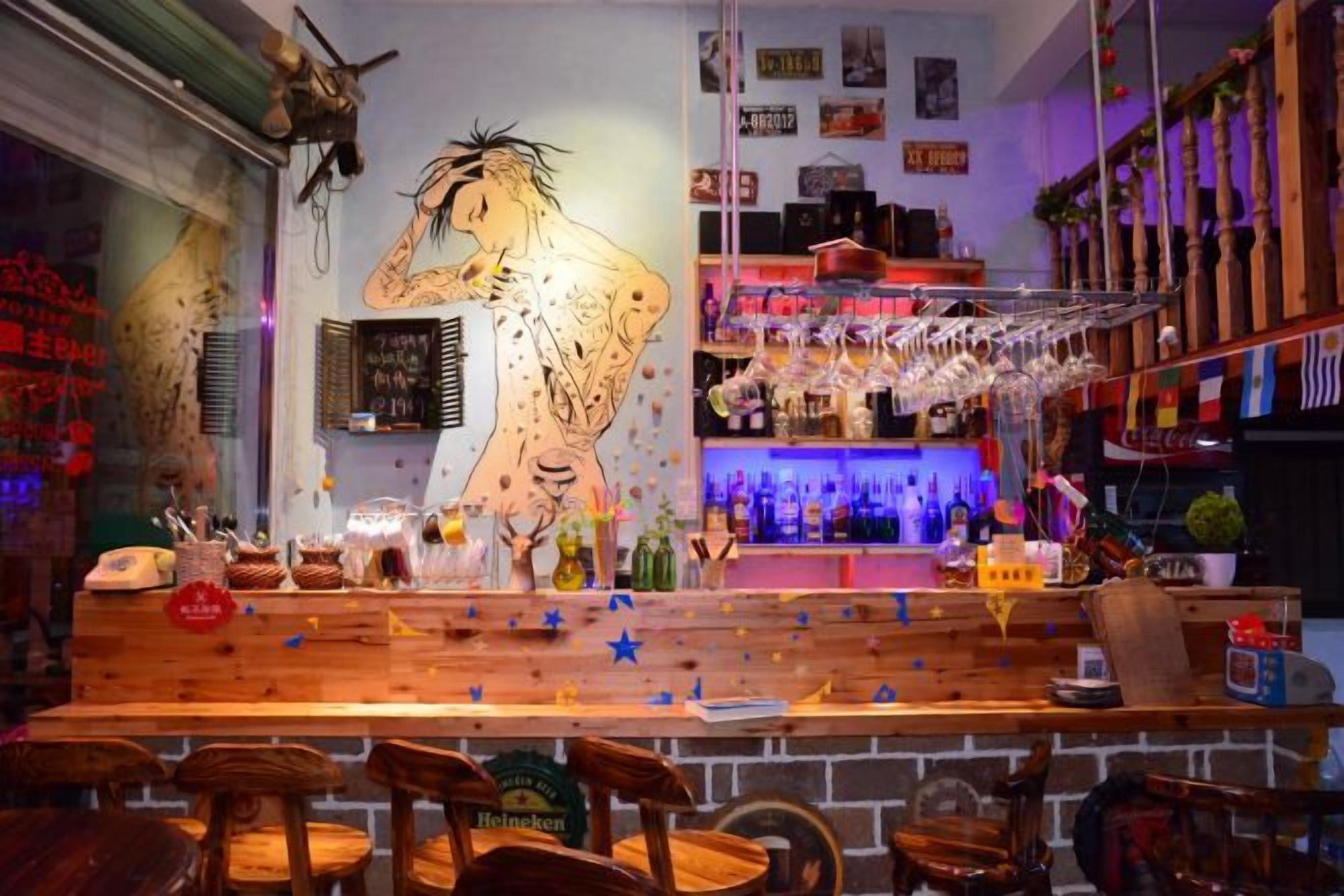 Zona de bar con taburetes de madera, un mural grande, estantes con botellas y una barra.