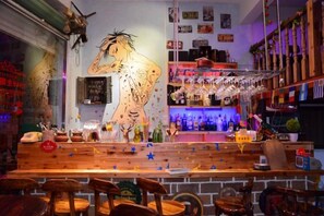 Eine Barbereich mit Holzhockern, einem großen Wandgemälde, Regalen mit Flaschen und einer Theke.