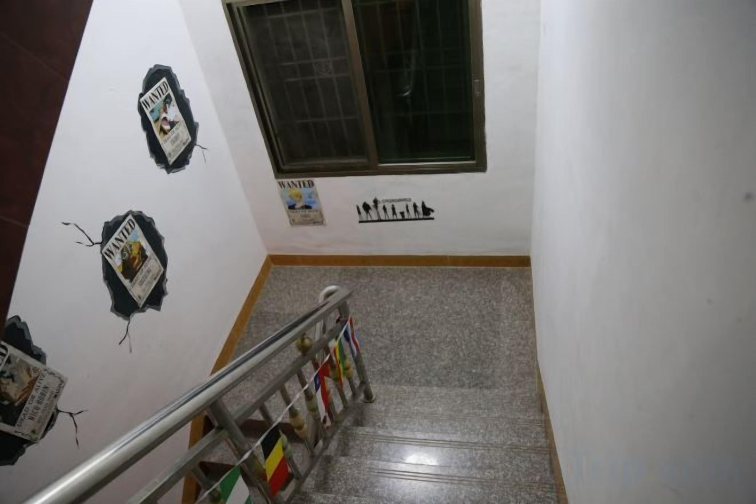 Una escalera con barandillas, una ventana y adornos en la pared, incluyendo un cartel de 'WANTED'.