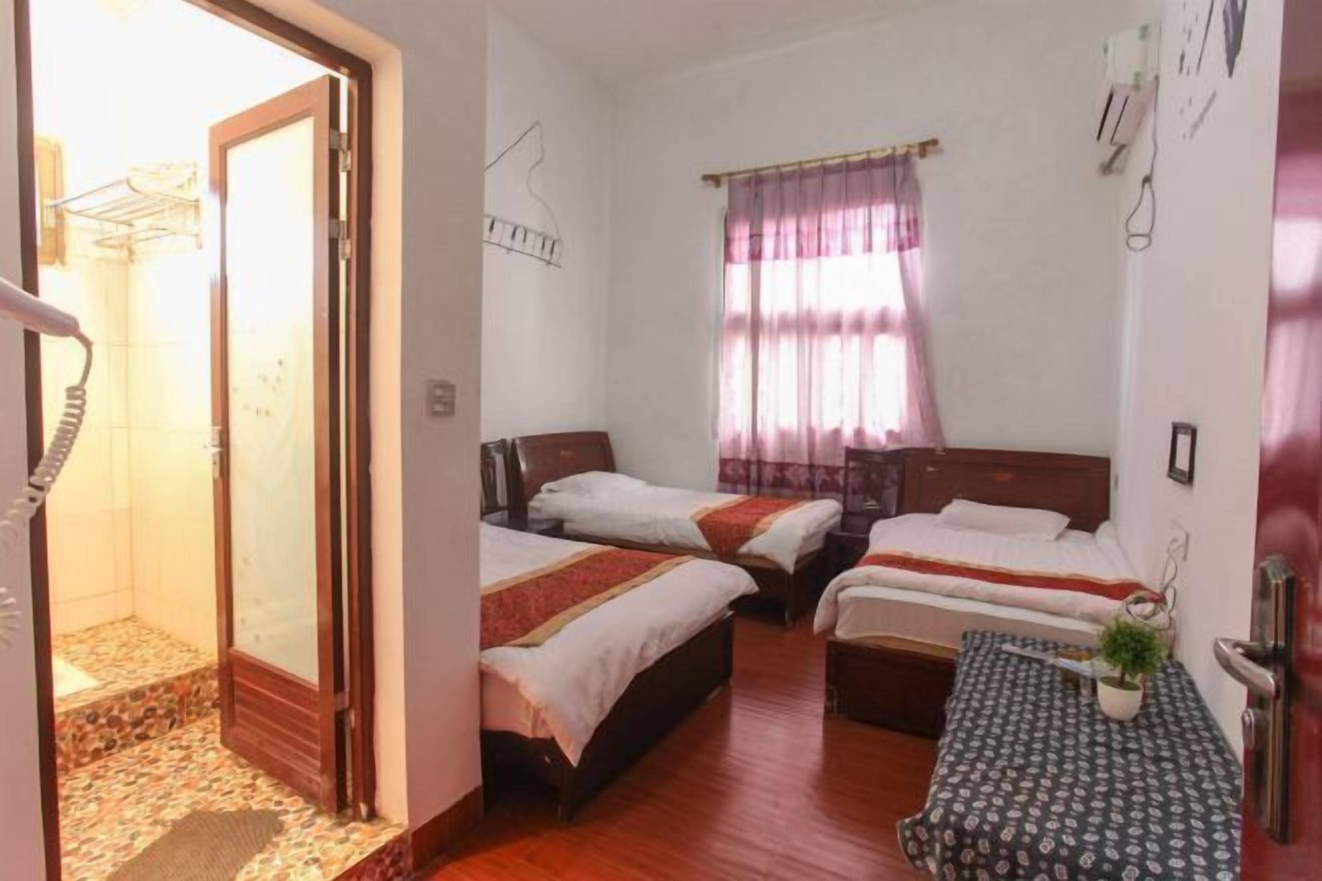 A hotel room with three single beds, a small table with a plant, and a shower area.