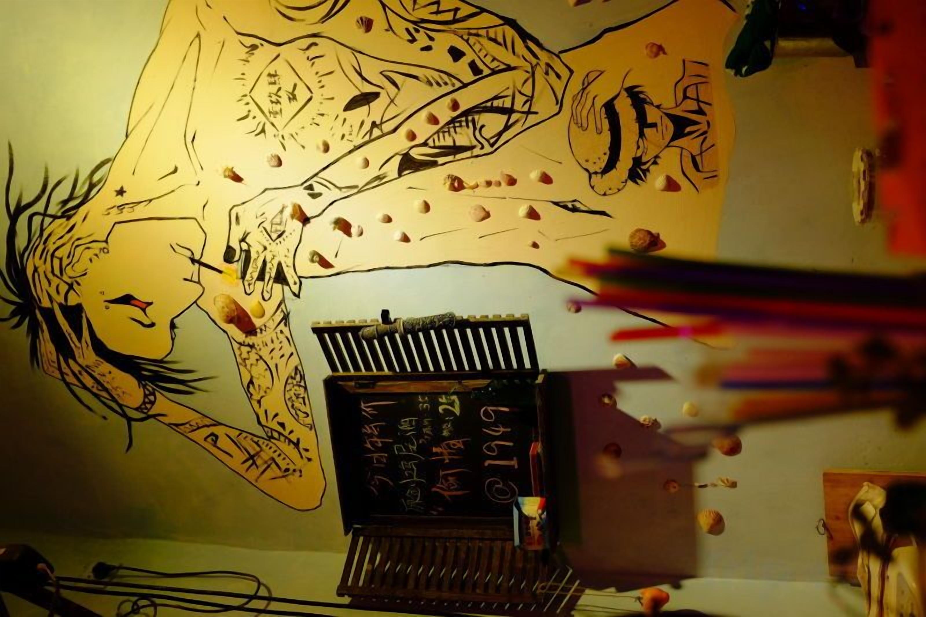 Quarto com um mural no teto, uma escrivaninha com computador e papéis espalhados.