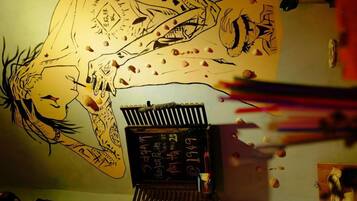 Quarto com um mural no teto, uma escrivaninha com computador e papéis espalhados.