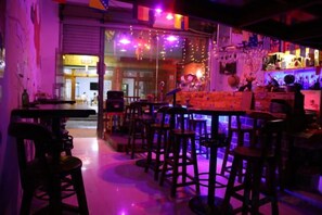Zona de bar con taburetes y una barra, una puerta visible que da al exterior y una pared con diversos objetos y adornos.