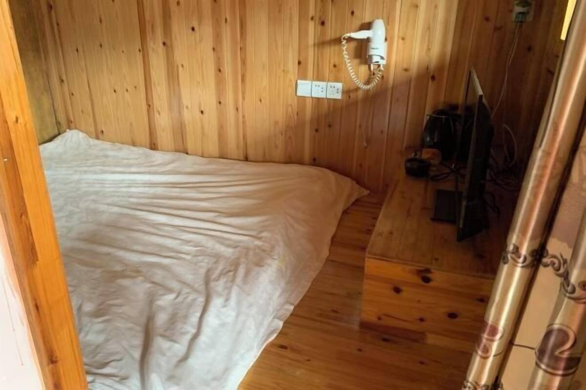 A wooden-paneled room with a bed, a wall-mounted hairdryer, and a power outlet.